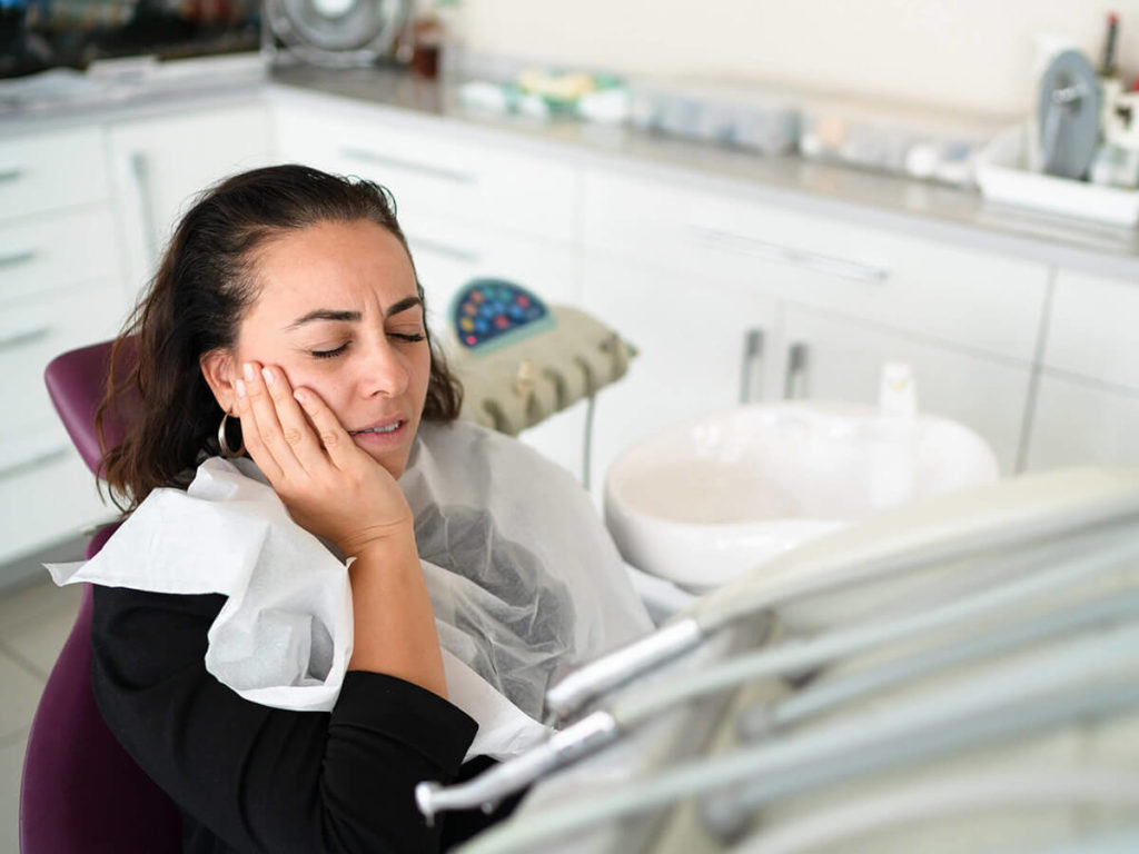 Patient in the dental chair gripping the side of her face in pain.