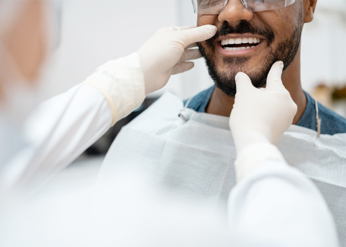 Smiling patient with the hands of a dental professional inspecting around his mouth.