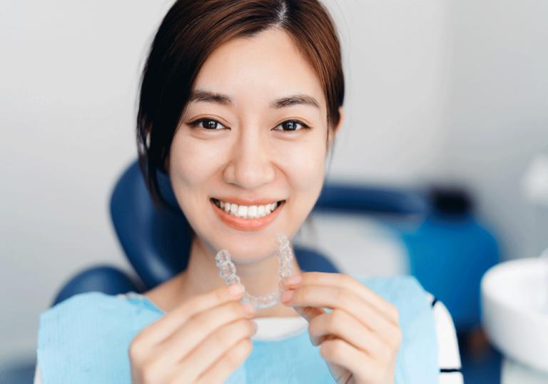 Woman smiling and holding Invisalign clear aligners