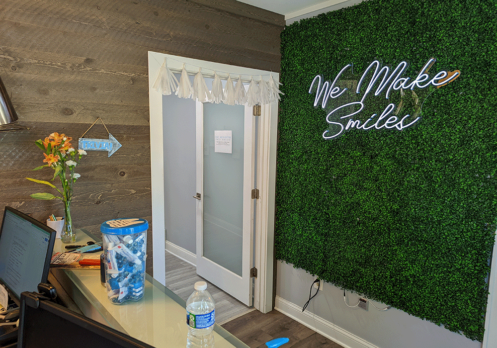 Photo of the front office area, with a grass wall and a neon sign that reads, "We make smiles" at Port Washington Family Dentistry in Port Washington, WI.
